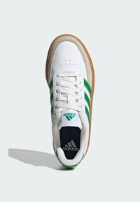 Bijela atletska cipela s ljubičastim i žutim prugama, suede akcentima i gumastom potplatom. Ima dizajn na vezivanje i urezane detalje s logom.