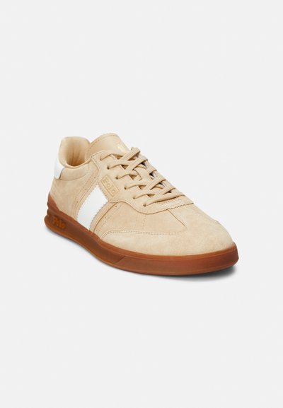 Beige suede sneaker with white synthetic stripes, round toe, lace-up closure, and brown rubber sole. Features "Polo" logo on the side.