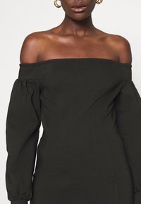 Black off-shoulder dress with puffed long sleeves, fitted bodice, and structured seams. Smooth fabric with minimal detailing.