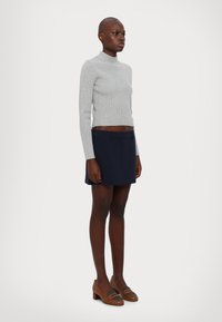 Maglione grigio a coste con collo alto e gonna A-line blu navy, abbinati a scarpe con tacco marroni con un accento grigio. Design semplice, silhouette aderente.