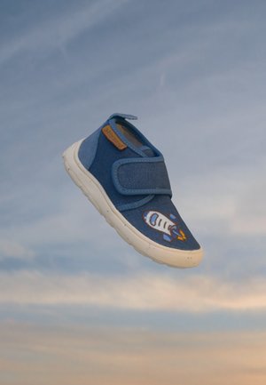 Blå børnesneaker med hvid sål og raketdesign svævende mod en skyet himmelbaggrund.
