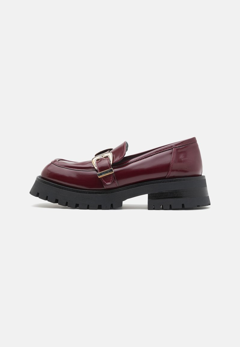 Burgundy patent leather loafers with a rounded toe, buckle detail, and chunky black treaded sole. Smooth texture and sleek design.