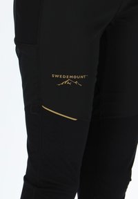 Black athletic pants with a side pocket, featuring gold accents and the "SWEDEMOUNT" logo. The fabric appears smooth and stretchy.