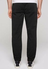Joggers neri a sigaretta con polsini elasticizzati, due tasche posteriori e una texture del tessuto liscia, abbinati a sneakers bianche e nere.