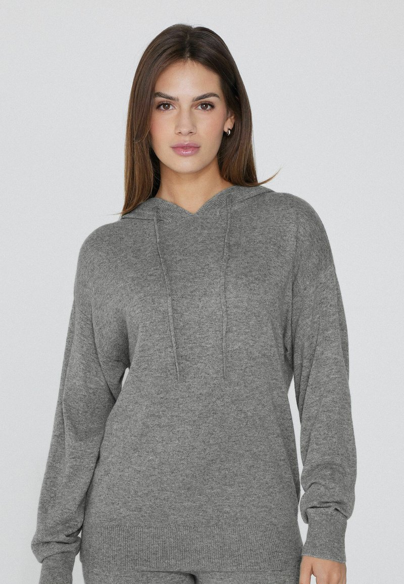 Sudadera gris de tela suave con un ajuste relajado, escote en V y mangas largas. Cuenta con cordones y puños y dobladillo acanalados.