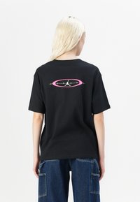 T-shirt en coton noir avec un logo graphique rose et vert au dos. Manches courtes et coupe décontractée. Texture lisse.
