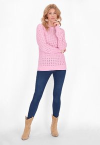 Ljusrosa stickad tröja med öppen stickning, ribbade ärmar, tillsammans med mörkblå leggings och tanfärgade ankelboots med texturerad design.