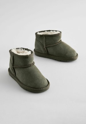 Kurze grüne Wildlederstiefel mit weicher weißer Fellfütterung und flacher Gummisohle. Mit gekreuzten Stickereien und einem Klettverschluss ausgestattet.