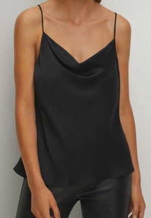 Woman wearing a black satin camisole with thin straps and a draped neckline, paired with black leather pants.