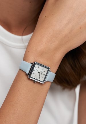 Square-shaped watch with a silver metal case, white dial, and blue leather strap. Features black hour markers and a crown on the side.