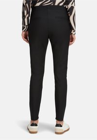 Czarne spodnie do kostek o gładkiej fakturze, z elastycznym pasem i dwoma tylnymi kieszeniami, zestawione z białymi i czarnymi trampkami.