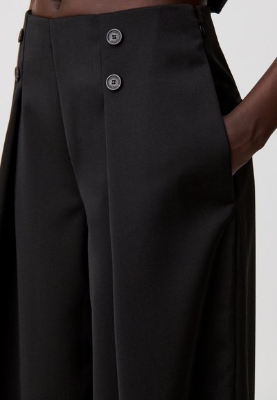 Pantalones anchos negros de tela suave con cintura alta, dos botones y bolsillos laterales. Líneas limpias con detalles entallados.