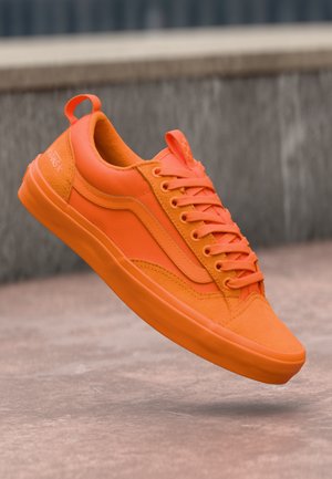 Zapatilla naranja con textura suave, que presenta una punta redondeada, seis ojetes y un tacón elevado. Logo de la marca exhibido en la parte trasera.