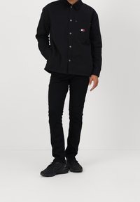 Svart skjorta med knappar, krage och bröstficka. Matchad med svarta byxor och svarta sneakers. Slät tyg, minimal design.