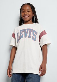 Camiseta blanca con acentos burdeos, con texto grande "LEVIT'S" en azul. Mangas cortas, corte relajado y material de algodón suave.