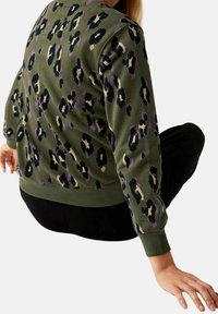 Sweatshirt imprimé léopard en vert olive avec des accents noirs, crème et lavande. Présente des poignets et un ourlet côtelés. Tissu doux, coupe décontractée.