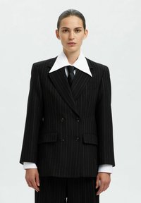 Črni blazirani dvoredni blazer z velikim belim ovratnikom in črno kravato. Ima oblazinjena ramena in žepne klape.