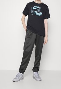 Černé tričko s modrým grafickým potiskem, doplněné tmavě šedými tepláky a šedými teniskami. Hladká látka a volný střih s elastickými manžetami.