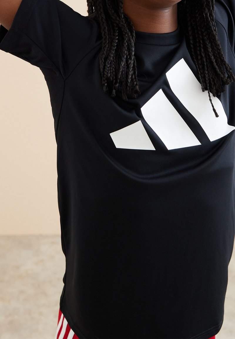 Camiseta atlética negra hecha de tela suave, con un gran logo blanco en el pecho. Mangas cortas y un ajuste holgado.