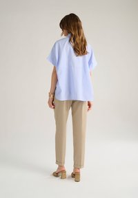 Camicia azzurra a righe con vestibilità ampia e maniche corte, abbinata a pantaloni beige a gamba affusolata. Design semplice senza motivi o accessori visibili.