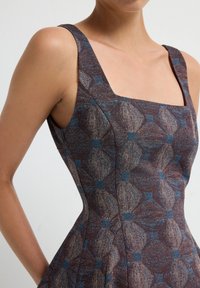 Robe à motif marron et bleu avec un col carré, des bretelles épaisses et une silhouette ajustée, comportant un tissu texturé et des détails de couture.