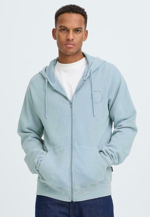 Hellblauer Kapuzenpullover mit Reißverschluss aus weichem Stoff, mit einer Fronttasche, Kordelzug an der Kapuze und einem dezenten Stickdetail auf der Brust.