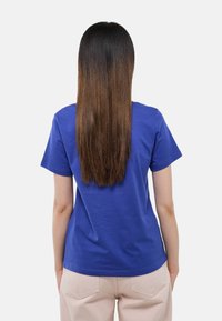 T-shirt à manches courtes, col rond, en coton bleu vif, présentant un design uni et une coupe décontractée, porté avec un pantalon beige clair.