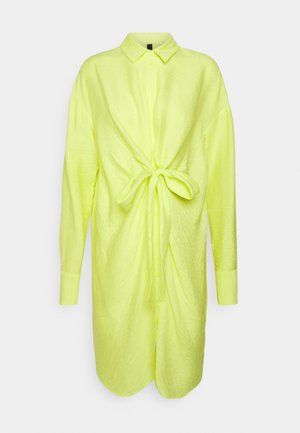 Camicia a maniche lunghe di un vivace giallo neon, con tessuto strutturato, chiusura frontale con bottoni e dettaglio annodato in vita.