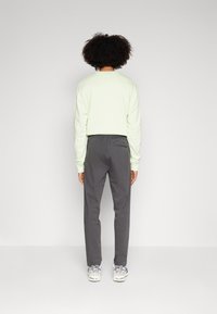 Lichtgroene sweatshirt en antracietgrijze broek, met een elastische tailleband. Het model staat met ontspannen armen, met de rug naar de camera gekeerd.