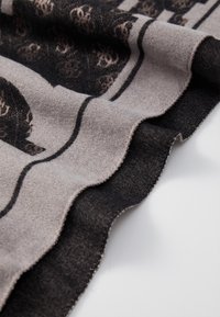 Beige és fekete színű kötött sál macska mintával. Az élei hullámos kialakításúak, puha tapintásúak és részletes varrás jellemzi őket.