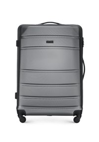 Maleta rígida gris con cuatro ruedas, líneas horizontales texturizadas, asas laterales y superior, y una placa con el logo frontal.