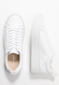 Ett par vita låga lädersneakers med vita snören och tjocka gummisulor, en sko sedd uppifrån, den andra från sidan.