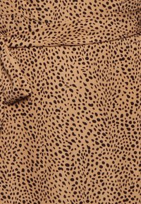 Tecido bege com um padrão de manchas pretas espalhadas, apresentando uma superfície texturizada e um detalhe amarrado no lado esquerdo.