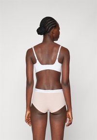 Hvit bralette med justerbare stropper kombinert med lyse rosa boyshorts. Livleggen har en "PIECES" logo i hvitt på en rosa bakgrunn.