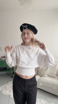 Svart basker med en pärlbåge, vit kort tröja med ribbad kant och svarta byxor med hög midja. Bakgrunden har mjuka inredningsdetaljer.