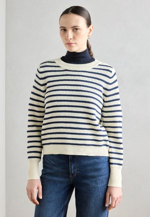 Maglione crema con righe orizzontali blu navy, colletto e polsini a coste, abbinato a jeans blu scuro. Texture morbida e vestibilità rilassata.