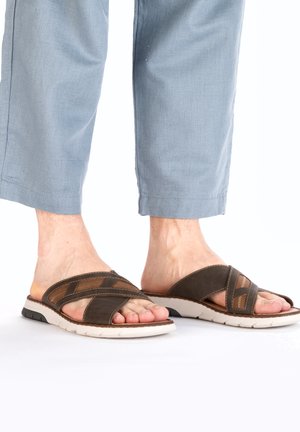 Black and brown slide sandals featuring cross straps and textured accents, with a white sole and flexible design, suitable for casual wear.
