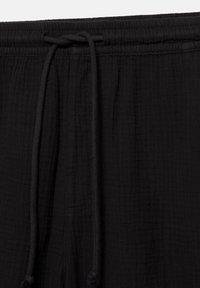 Taille de pantalon en tissu noir texturé avec élastique et cordons noués suspendus à l'avant.