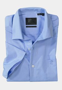 Camisa de vestir de color azul claro, plegada, hecha de algodón. Presenta un cuello clásico, cierre de botones y un logotipo bordado en el bolsillo.