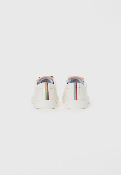 Un paio di sneakers bianche a basso profilo con striscia verticale multicolore sulle collo delle scarpe, viste da dietro su uno sfondo chiaro e semplice.