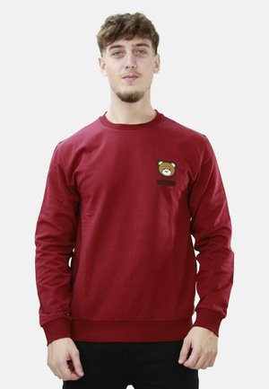 Felpa rossa in cotone con maniche lunghe, polsini a costine e una patch di un orsetto dei cartoni animati sul lato sinistro del petto con il testo "Moschino" sotto di essa.