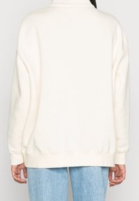 Krämfärgad oversize sweatshirt med hög krage, ribbade muddar och nederkant. Mjuk textur, minimalistisk design och inga synliga mönster.