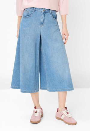 Lyseblå denim culottes med vide ben, båret med pink og hvide sneakers, vist fra taljen til anklerne mod en hvid baggrund.