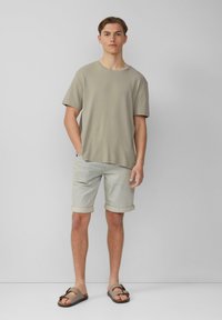 T-shirt gris à manches courtes à côtes associé à un short en denim clair retroussé au bord et des sandales marron avec un détail de boucle.