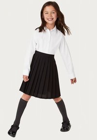 Camisa blanca abotonada, falda negra plisada, calcetas grises hasta la rodilla y zapatos negros estilo Mary Jane. Niño posando con brazos y piernas en movimiento.