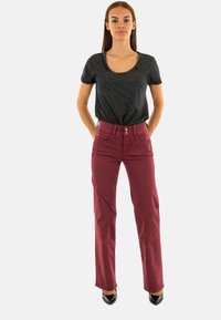 Pantalones burdeos de corte ajustado y cinco bolsillos, combinados con una camiseta de manga corta a rayas en blanco y negro. Tacones altos completan el conjunto.