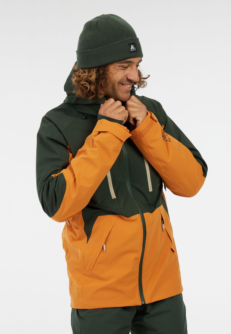 Grüne und orange wasserdichte Jacke mit einem Reißverschluss, verstellbarem Kapuze und zwei Fronttaschen. Warme Strickmütze in Dunkelgrün.