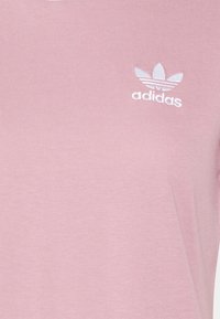 Rožinė medvilninė marškinė su balta siuvinėta Adidas logo ir raukšlėta tekstūra. Paprastas dizainas su trumpomis rankovėmis ir apvaliu kaklu.