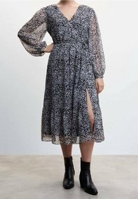 Zwarte bloemen midi-jurk met een V-hals, doorzichtige lange mouwen, geplooide textuur, tailleband, zijsplit en gedragen met zwarte enkelbootjes.