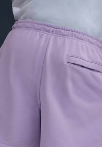 Pantalones cortos deportivos lilas hechos de un tejido suave y liso. Cuentan con una cintura elástica y un pequeño bolsillo trasero para almacenamiento.